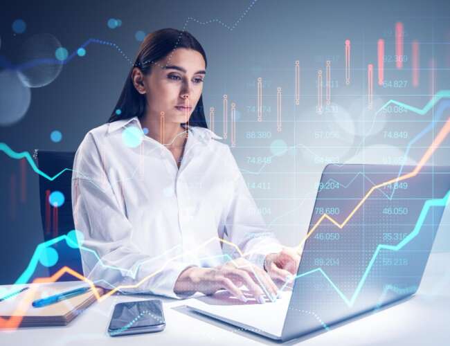 joven-mujer-negocios-atractiva-sentada-escritorio-oficina-usando-computadora-portatil-grafico-divisas-brillante-fondo-bokeh-borroso-finanzas-comerciales-concepto-mercado.jpg